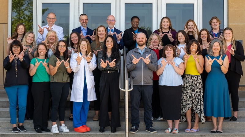 The faculty, fellows, nurses, pharmacists, and other staff of the UW Department of Ob-Gyn Division of Gynecologic Oncology stand together on a staircase, all making a W sign with their hands to symbolize Wisconsin